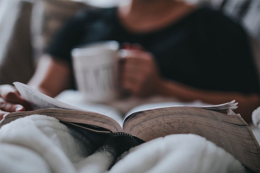 A resident reading a book in bed with a cup of coffee